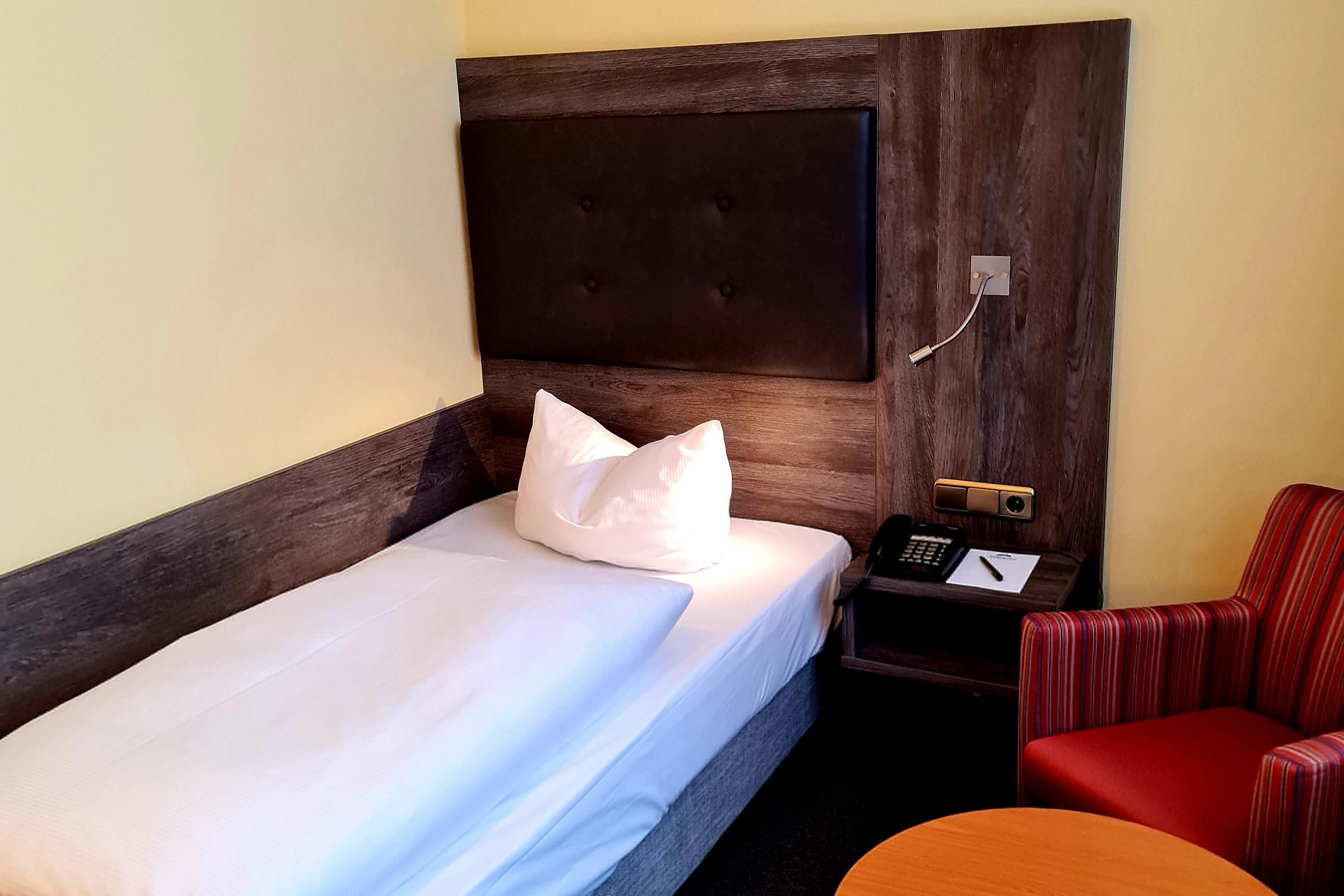 A hotel room with a bed, a bedside table with a phone, and a red chair.