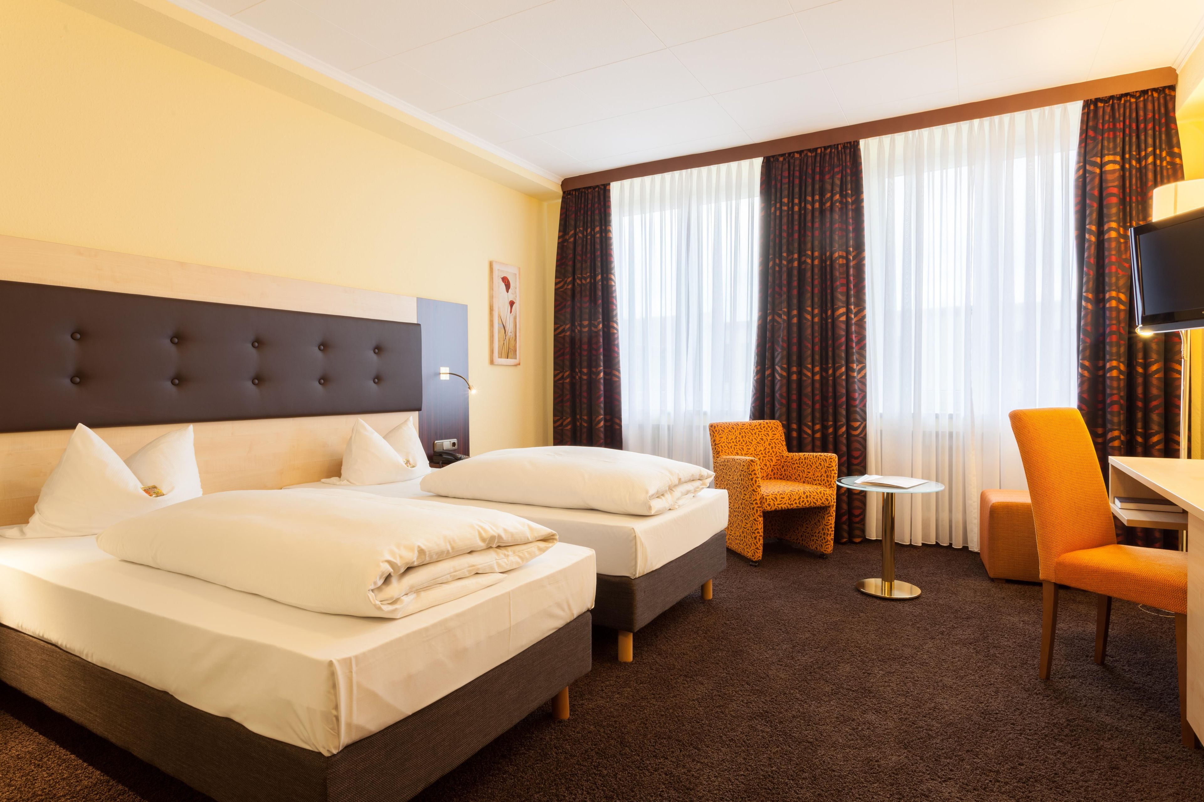 A hotel room with two beds, a small table, a chair, and a TV.