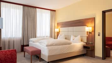 Una habitación de hotel con una cama grande, dos lámparas de noche, un cabecero de madera, una silla roja y una mesita.