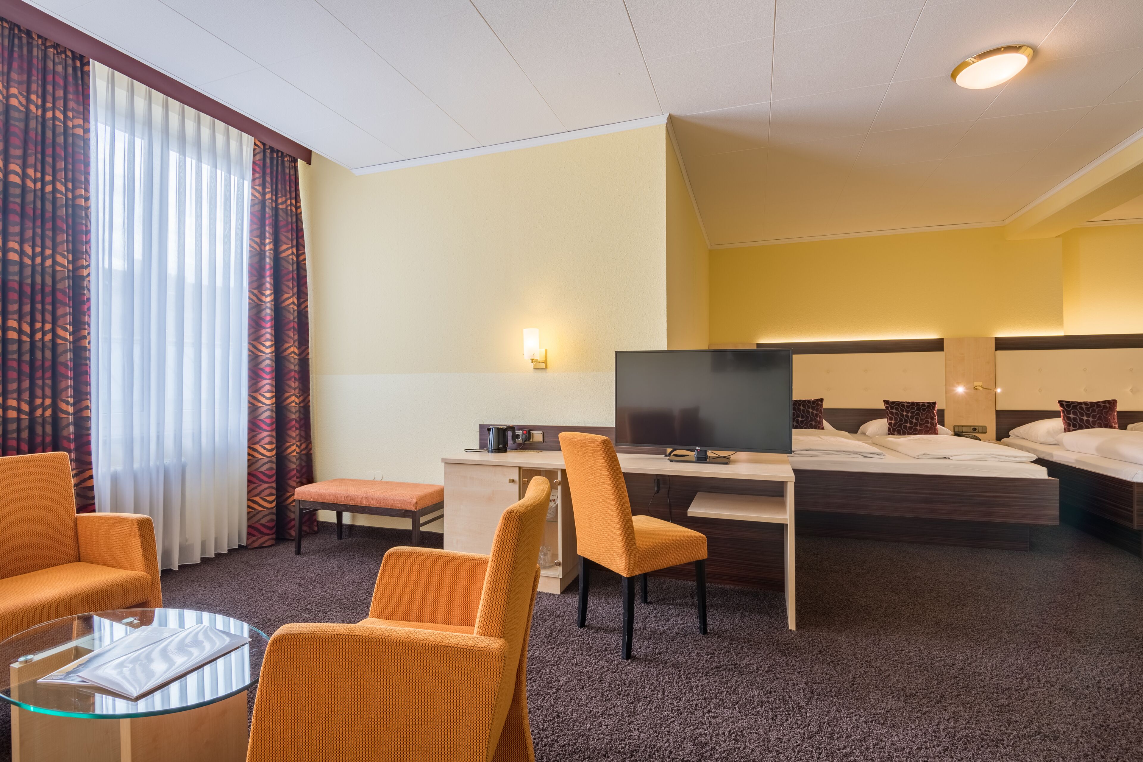 Quarto de hotel com cama, escrivaninha, cadeira, televisão e sofá.
