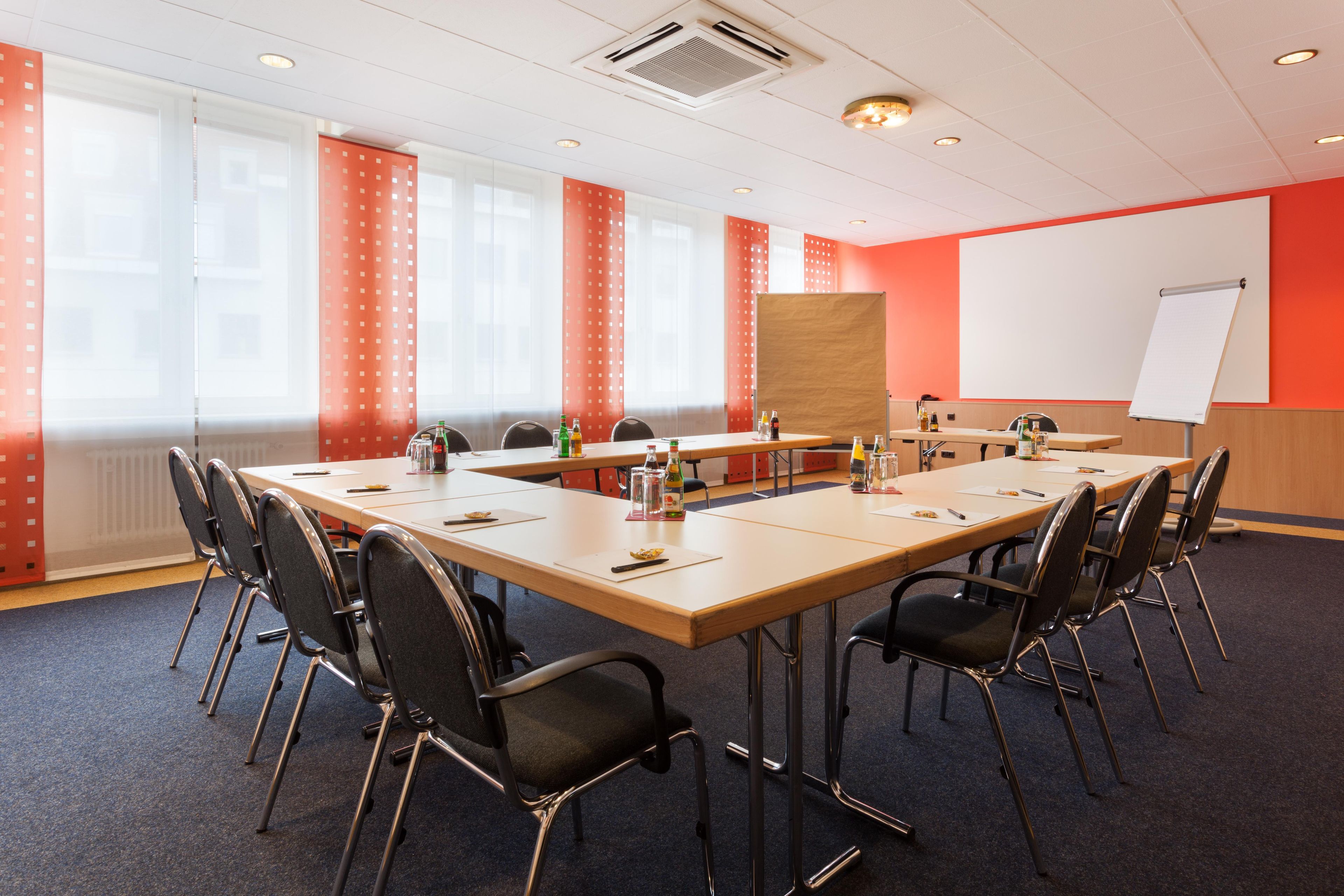 Ein Konferenzraum mit einem langen Tisch, Stühlen, einer Whiteboard-Tafel und einer Projektionsleinwand.