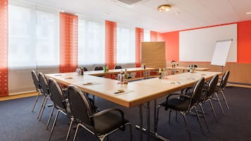 Ein Konferenzraum mit einem langen Tisch, Stühlen, einer Whiteboard-Tafel und einer Projektionsleinwand.