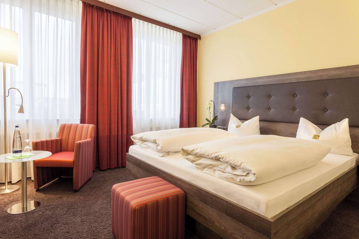 Ein Hotelzimmer mit einem großen Bett, einem Sessel, einem kleinen Tisch und einer Lampe.