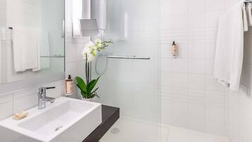 Ein modernes Badezimmer mit einem weißen Waschbecken, einer Duschkabine aus Glas und einer Orchidee im Topf.