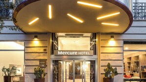 Exterior del Hotel Mercure con una entrada moderna, plantas en macetas y una fachada bien iluminada.