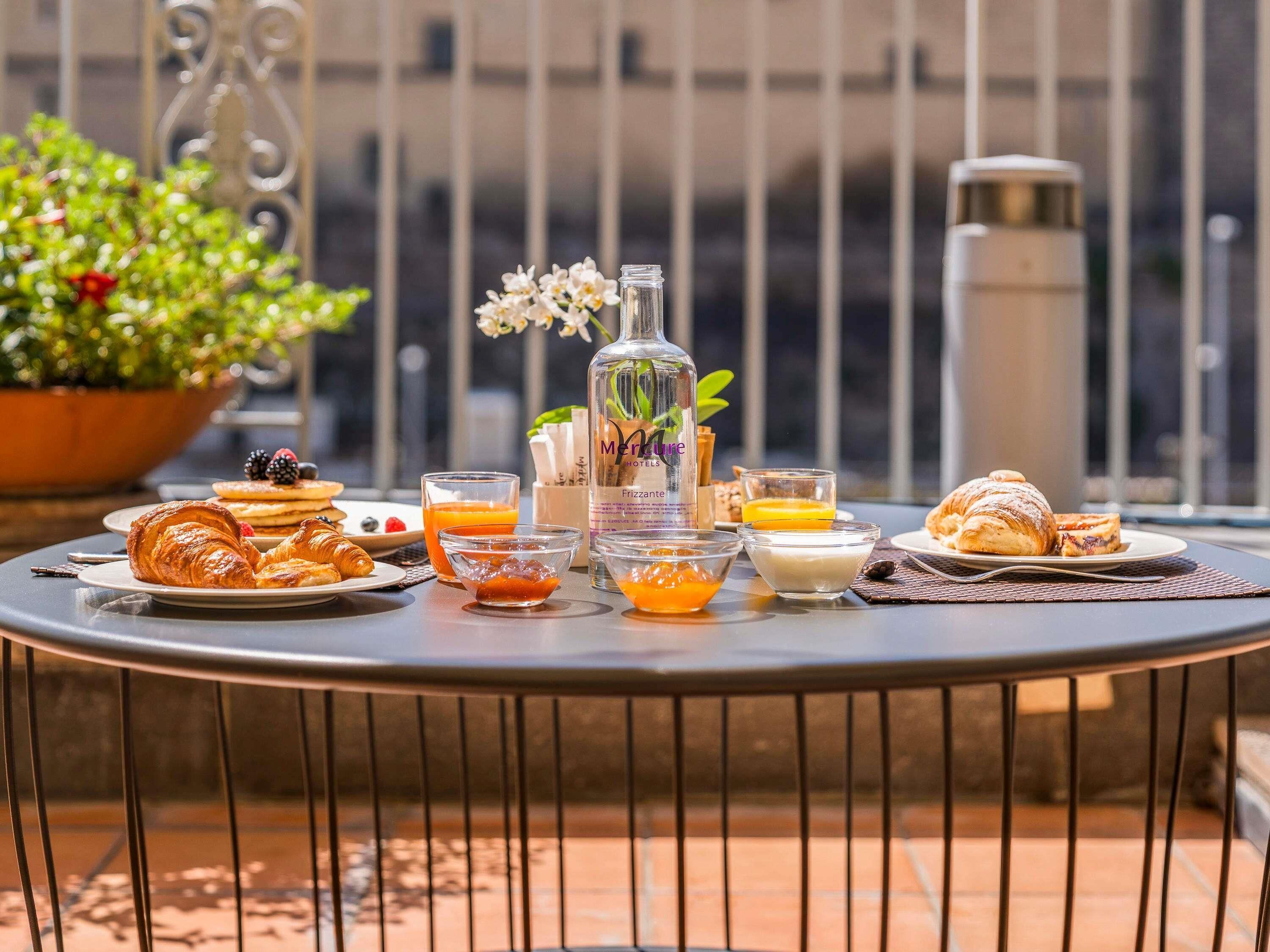 A table with breakfast items including croissants, pancakes, and a bottle of Frizzante.
