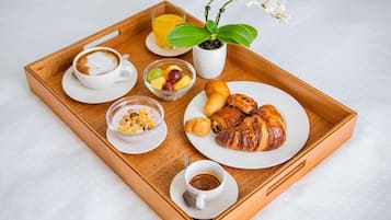 Una bandeja de madera con alimentos para el desayuno, incluyendo croissants, fruta, café y una pequeña planta.