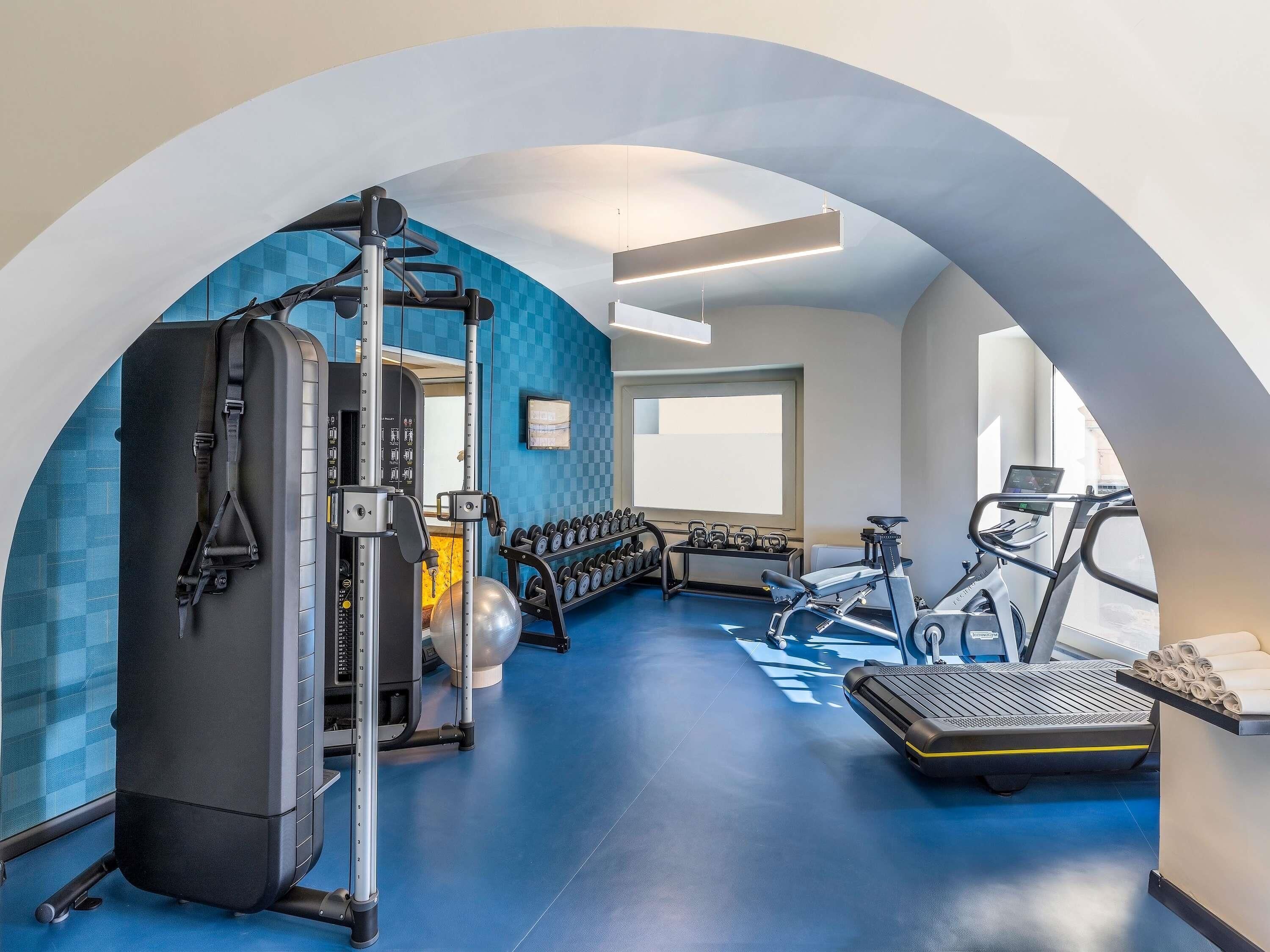 A gym with a squat rack, dumbbells, an elliptical, and a treadmill.