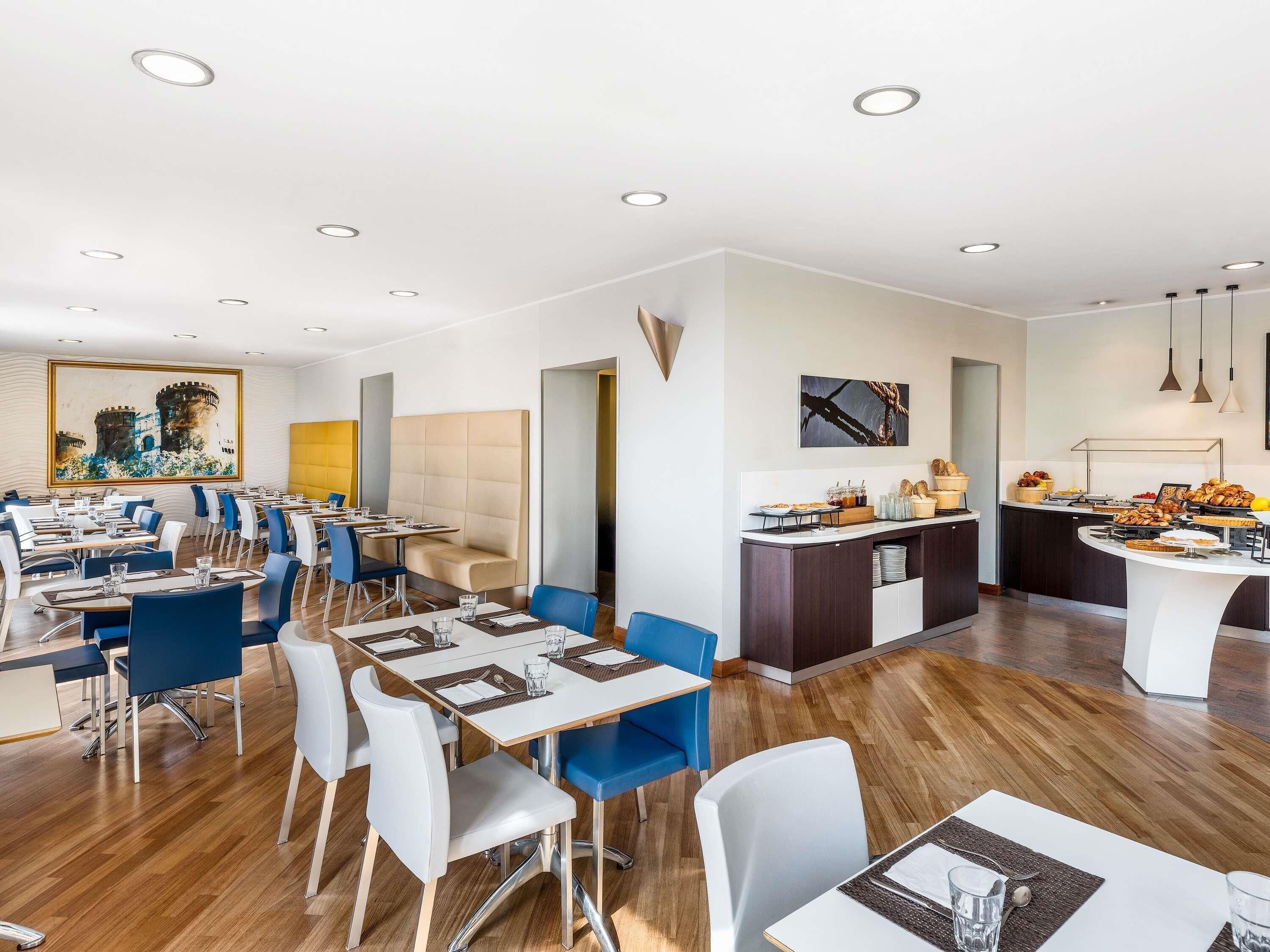 Un comedor moderno con varias mesas y sillas, una barra de buffet con diversos alimentos y un cuadro grande en la pared.