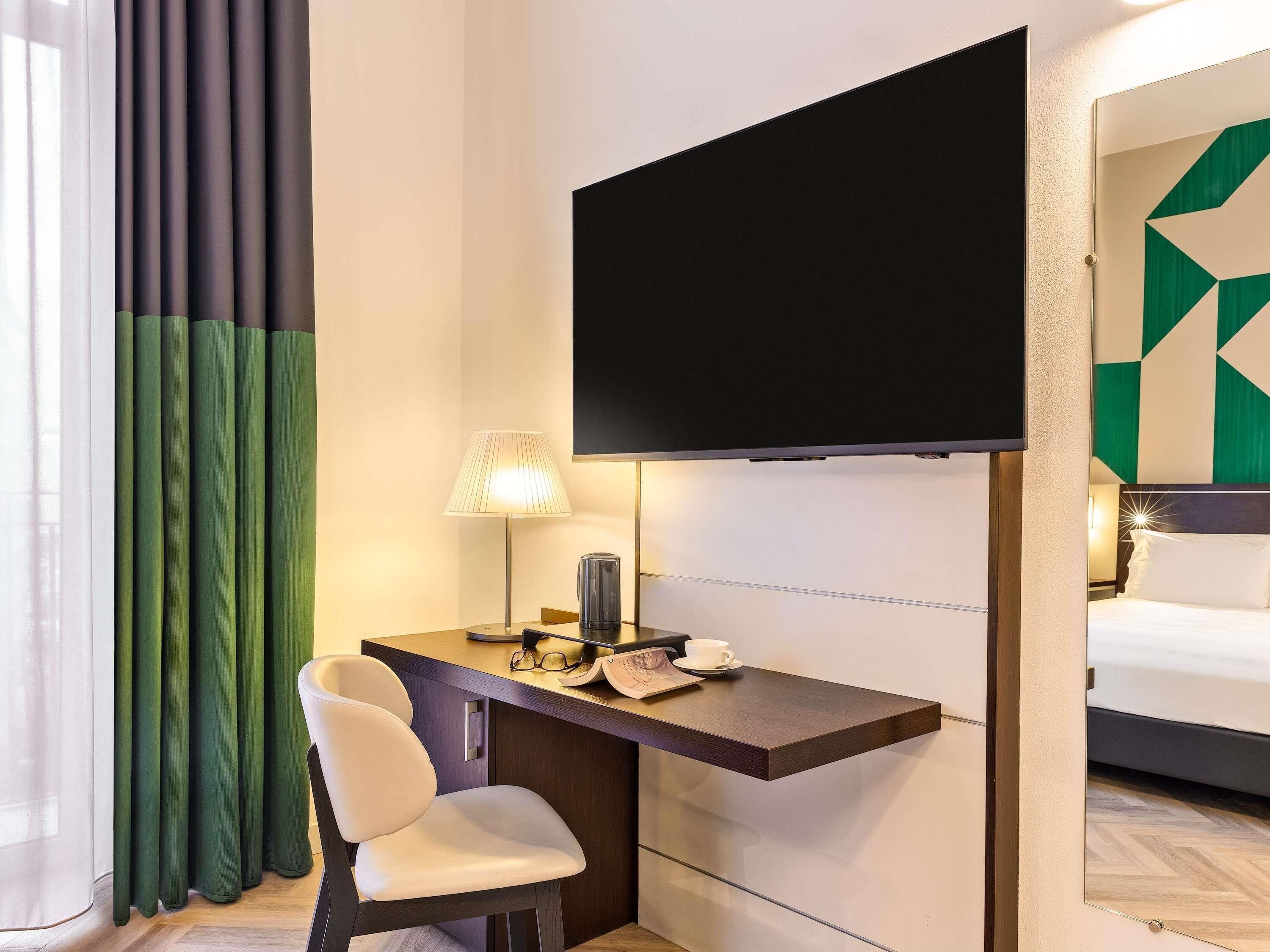 Una camera d'albergo con scrivania, sedia, televisore, lampada e letto.