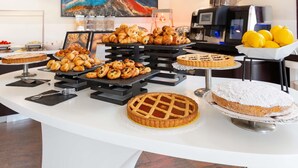 Un bufé con diversas pastelerías y pasteles, una máquina de café y una pintura de una montaña.