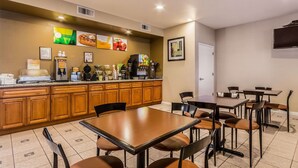 Un'area ristorazione in hotel con mobili a legno, un angolo caffè e diversi tavoli e sedie.