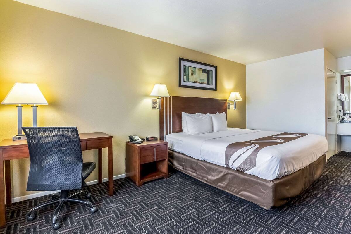A hotel room with a bed, desk, chair, and two bedside lamps.
