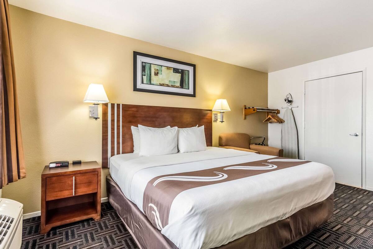 A hotel room with a large bed, two bedside lamps, a framed picture on the wall, a wooden nightstand, and a door with a towel rack.