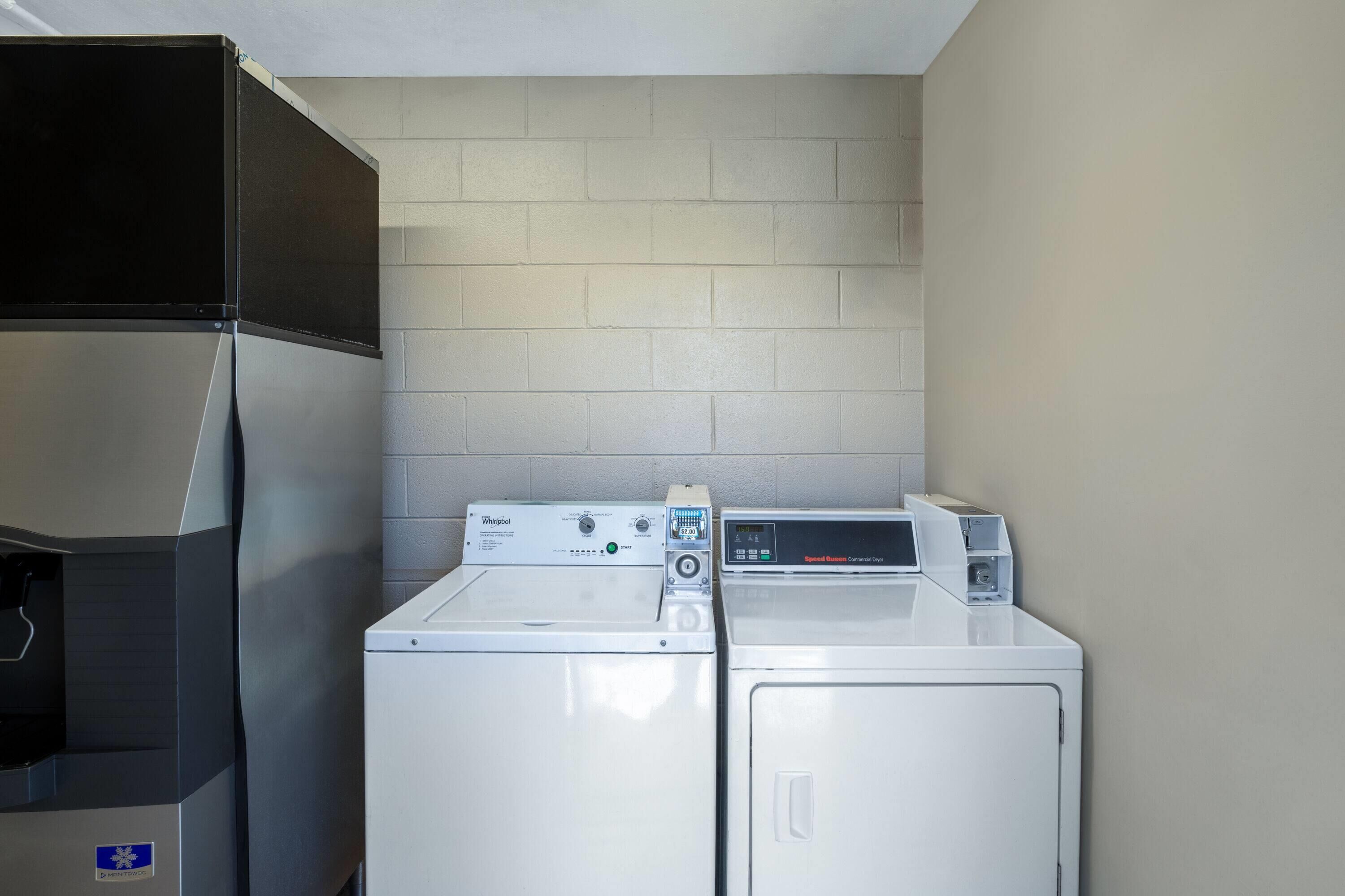 A laundry room with two white washers and dryers, a black refrigerator, and a tiled wall.