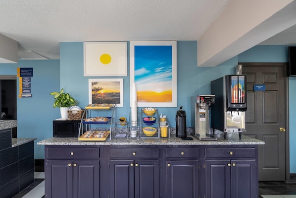 A kitchen with a granite countertop, dark cabinets, and a coffee machine.