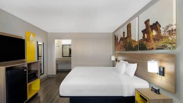 A hotel room with a bed, a TV, a microwave, a mini-fridge, a nightstand, and a wall-mounted lamp.