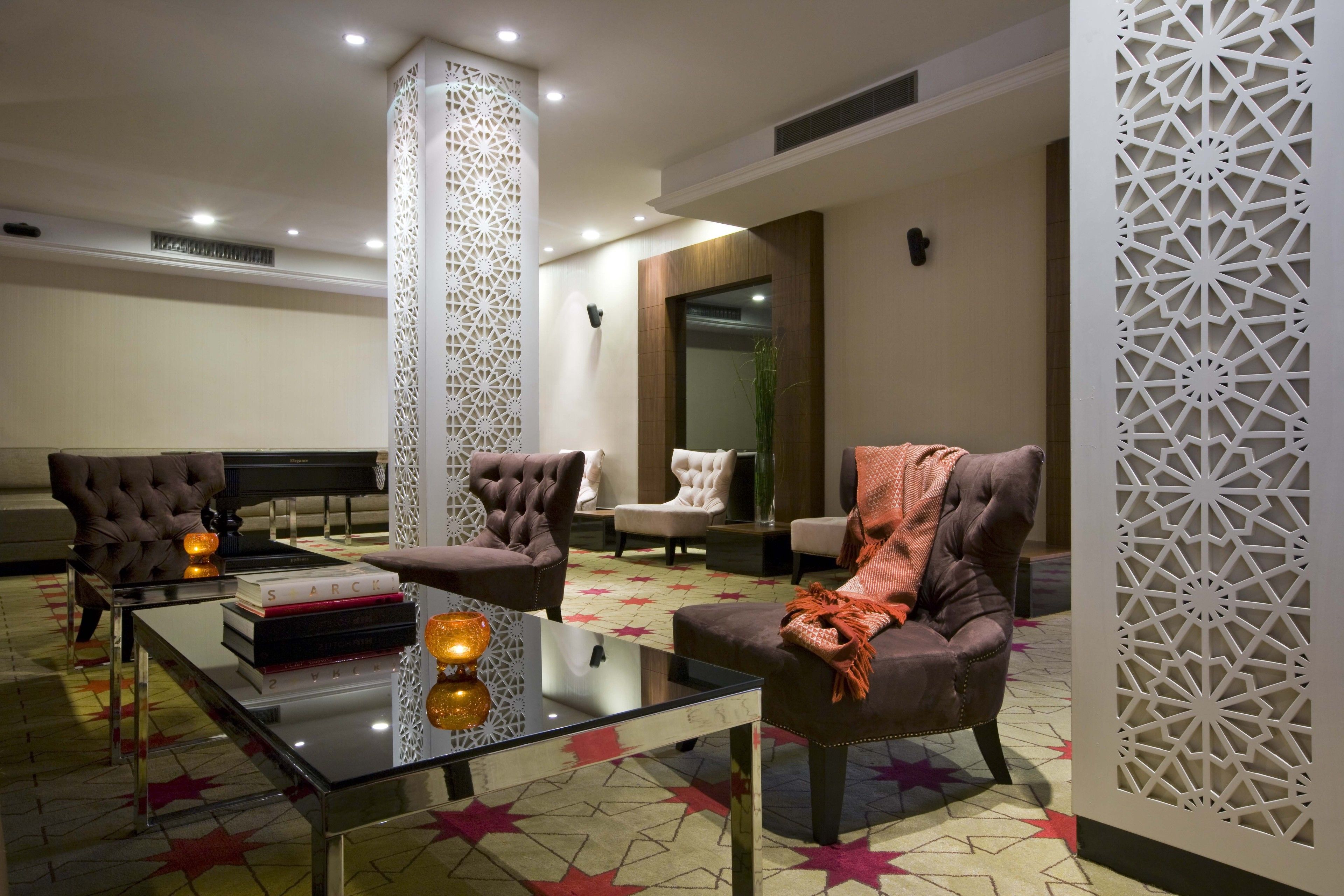 A modern lounge area with leather armchairs, a glass coffee table, and decorative elements like a tall pillar and intricate wall panels.