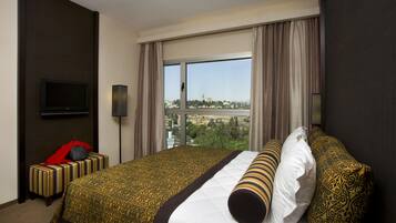 Habitación de hotel con una cama grande, un televisor montado en la pared y vistas a un paisaje urbano a través de la ventana.