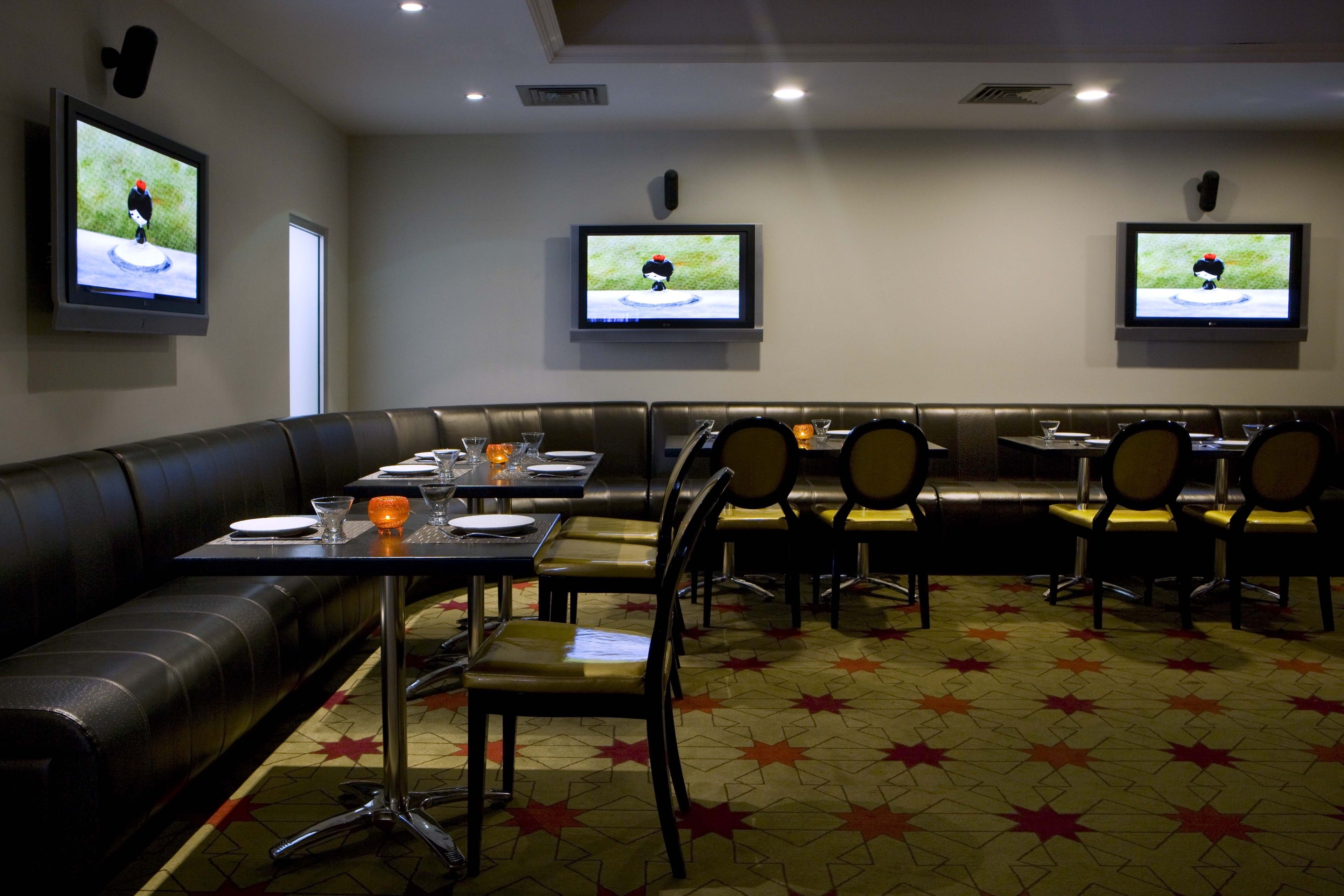 Ein Restaurant mit einer Sitzecke, Tischen und Fernsehern, die ein Spiel zeigen.