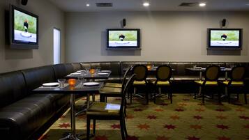 Ein Restaurant mit einer Sitzecke, Tischen und Fernsehern, die ein Spiel zeigen.