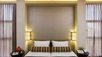 A hotel room with a large bed, two bedside tables, a potted plant, and a wall-mounted lamp.