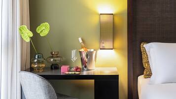 Une chambre d’hôtel avec un bureau en bois, une chaise, un lit agrémenté d’oreillers à motifs, un luminaire fixé au mur et une plante décorative.