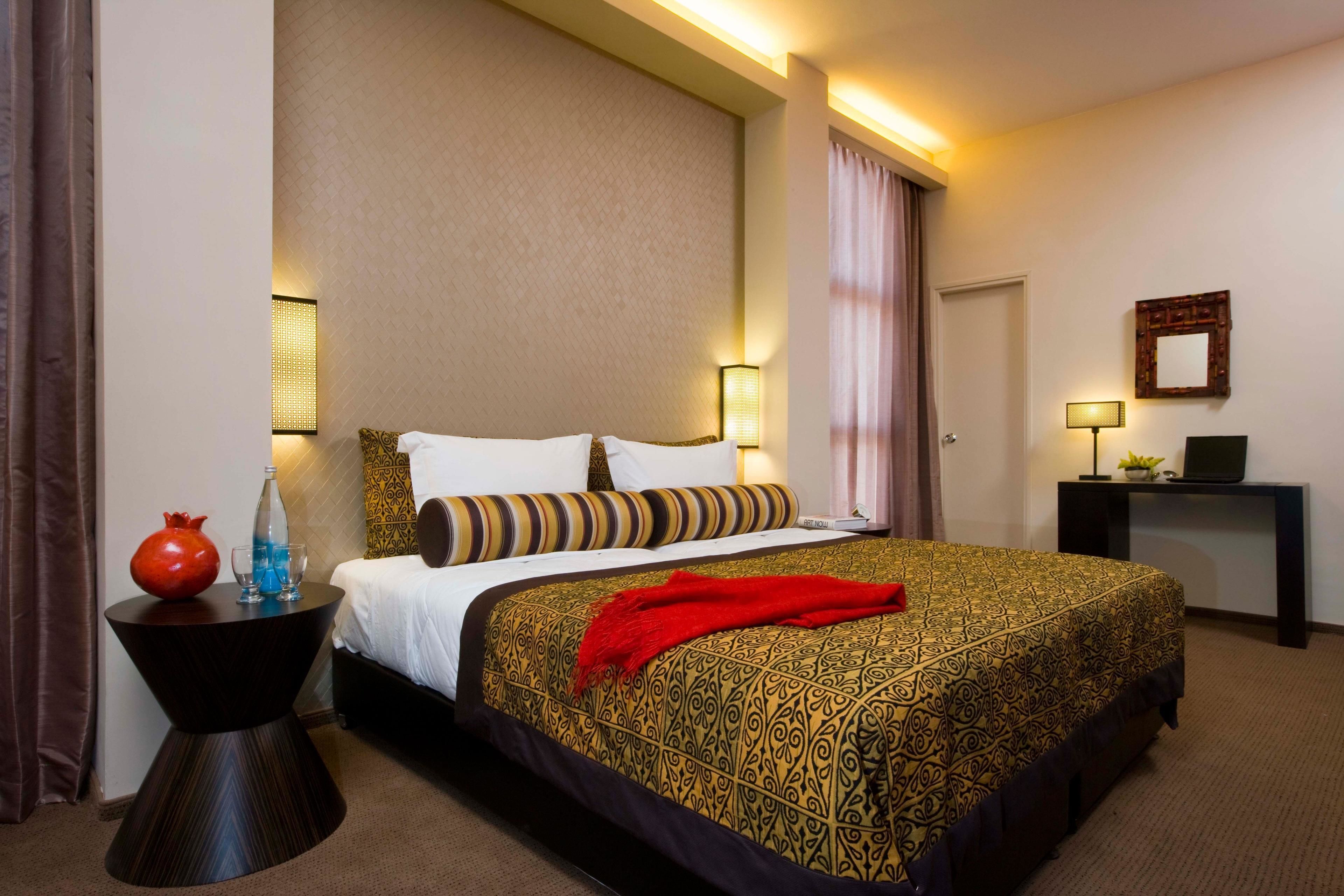 Una habitación de hotel con una cama grande, una mesita de noche, un escritorio y un espejo.