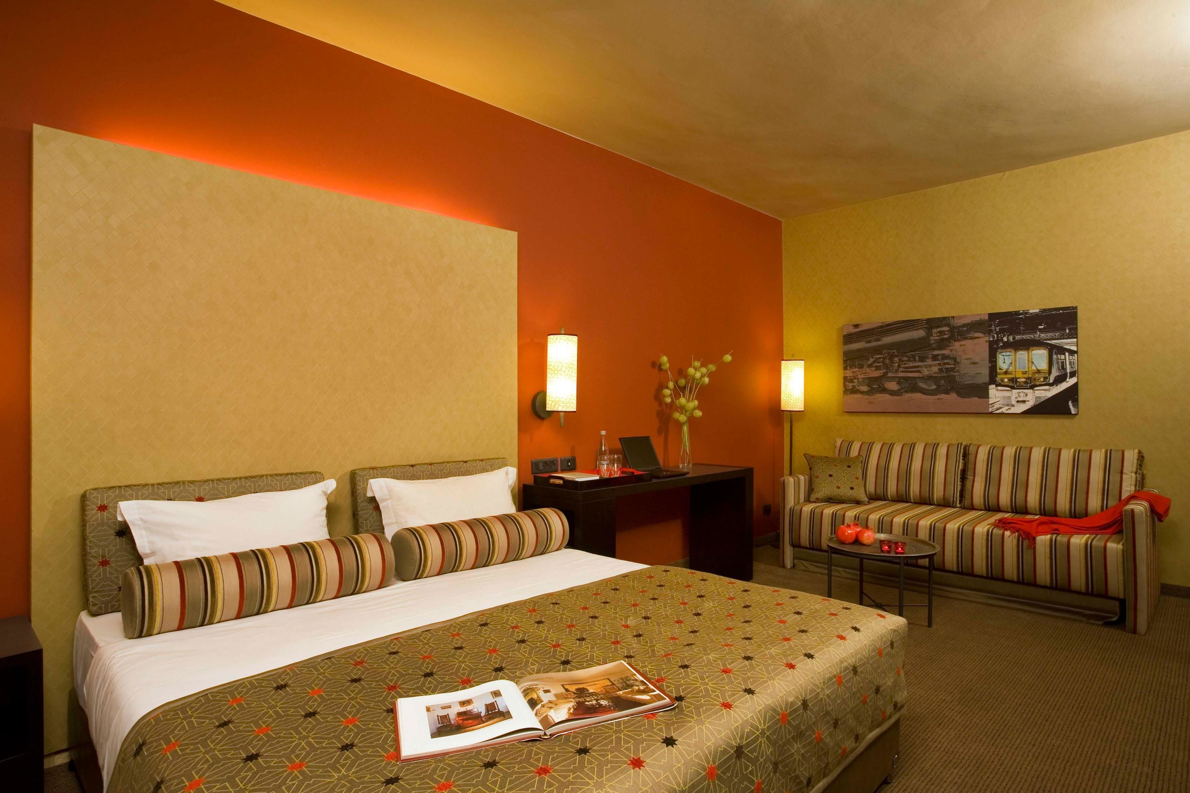 A hotel room with a bed, a sofa, a small table, and a desk with a lamp.