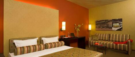 A hotel room with a bed, a sofa, a small table, and a desk with a lamp.
