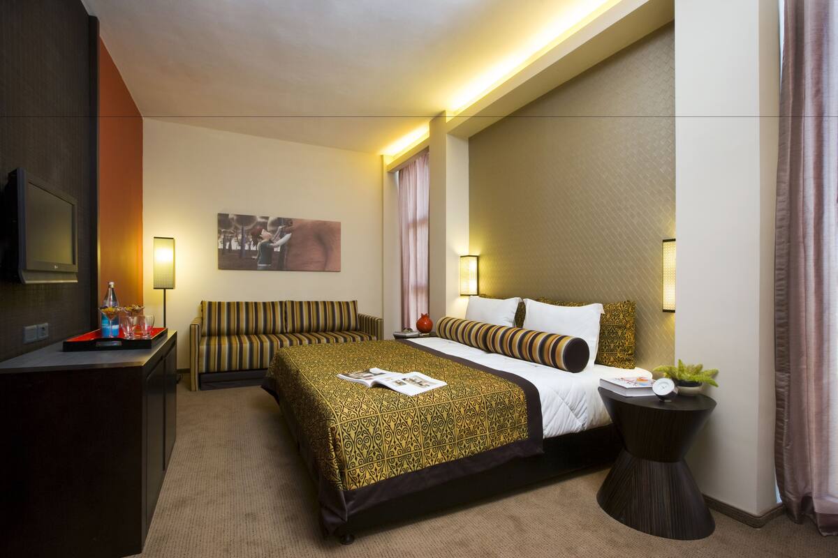 Une chambre d’hôtel avec un grand lit, des tables de chevet, un bureau, une télévision et un canapé.