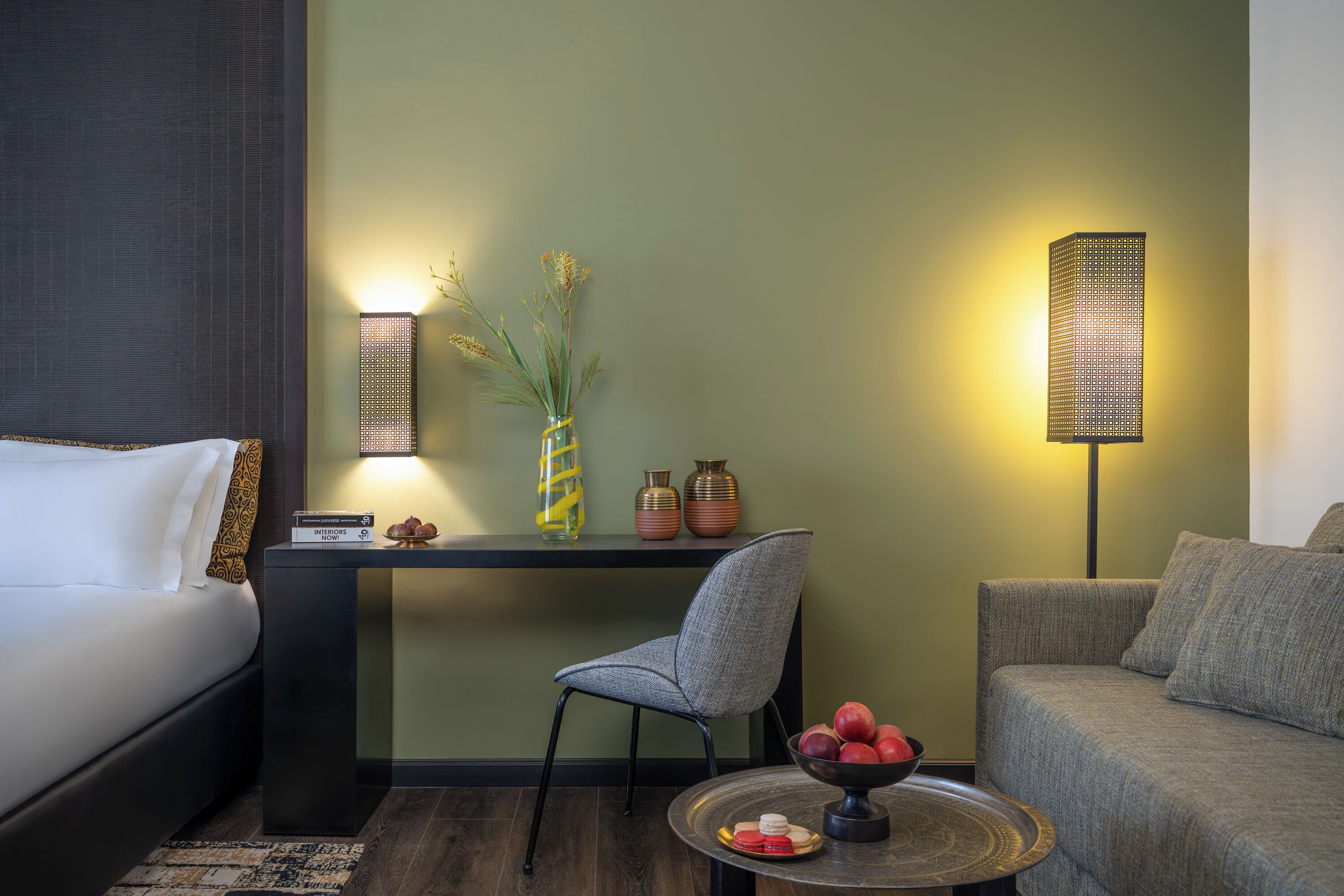 Habitación de hotel con una cama, un escritorio, una silla, un sofá, una lámpara y una pequeña mesa con un frutero.