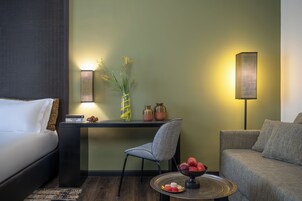 Habitación de hotel con una cama, un escritorio, una silla, un sofá, una lámpara y una pequeña mesa con un frutero.