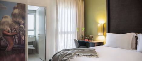 A hotel room with a large bed, a desk with a lamp, and a painting on the wall.