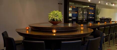 Zona de bar con una mesa redonda, sillas y una planta en maceta.