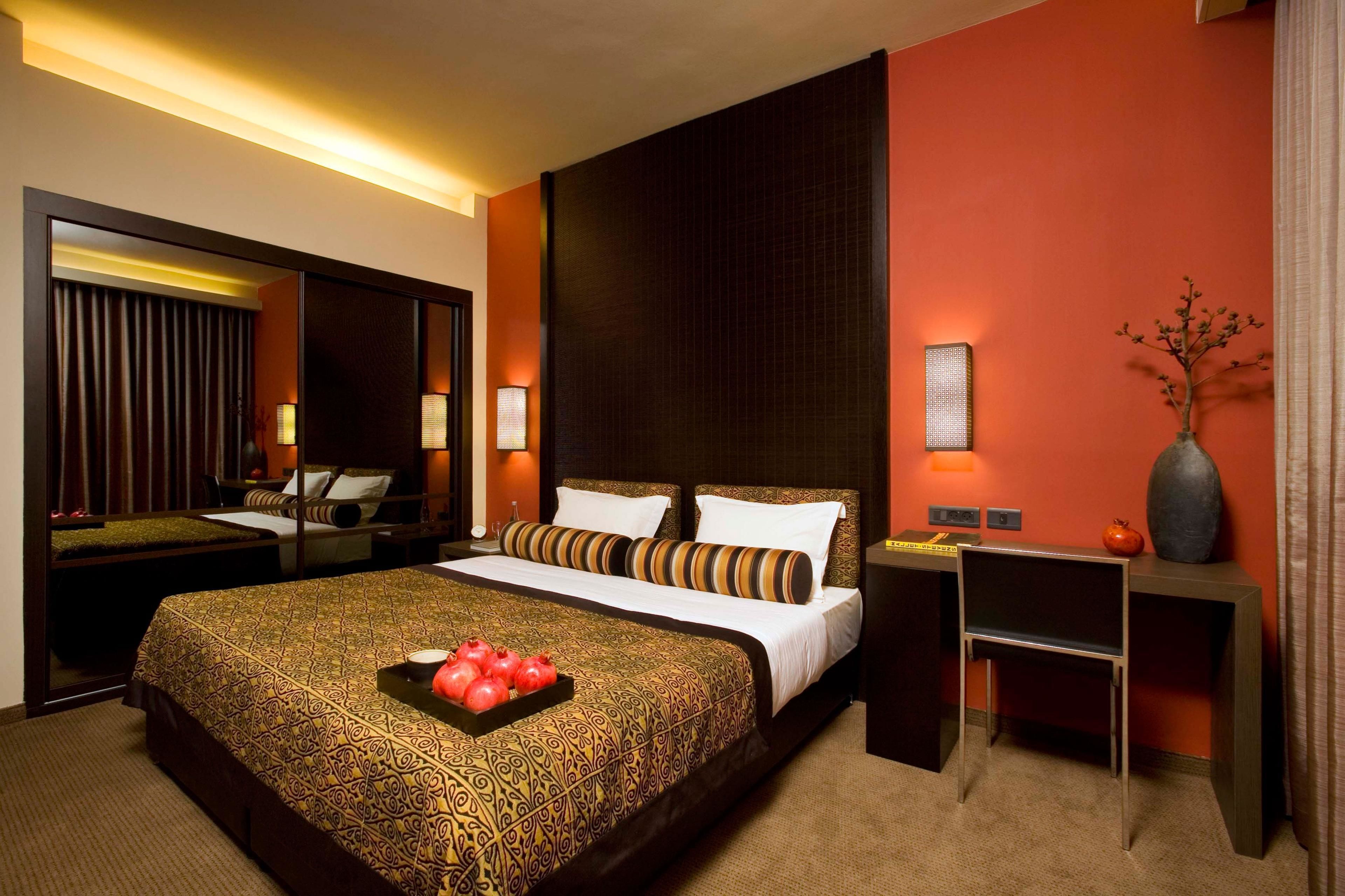 A hotel room with a large bed, a desk, a chair, a vase, and a potted plant.