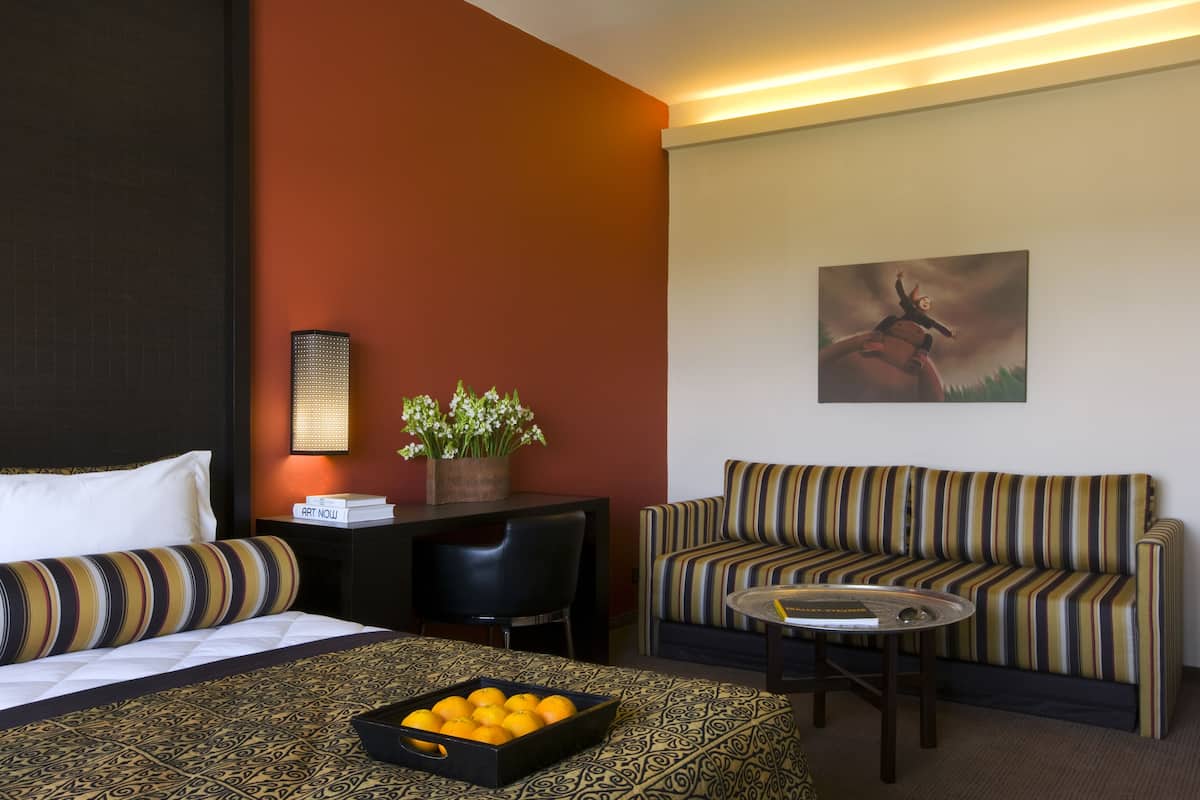 Une chambre d’hôtel avec un lit, un canapé, un bureau, une chaise, une petite table et un tableau au mur.