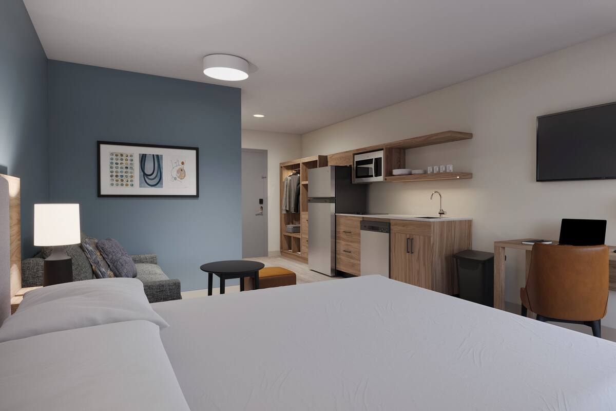 Una habitación de hotel moderna con una cama grande, un escritorio con computadora, un microondas y un televisor de pantalla plana.
