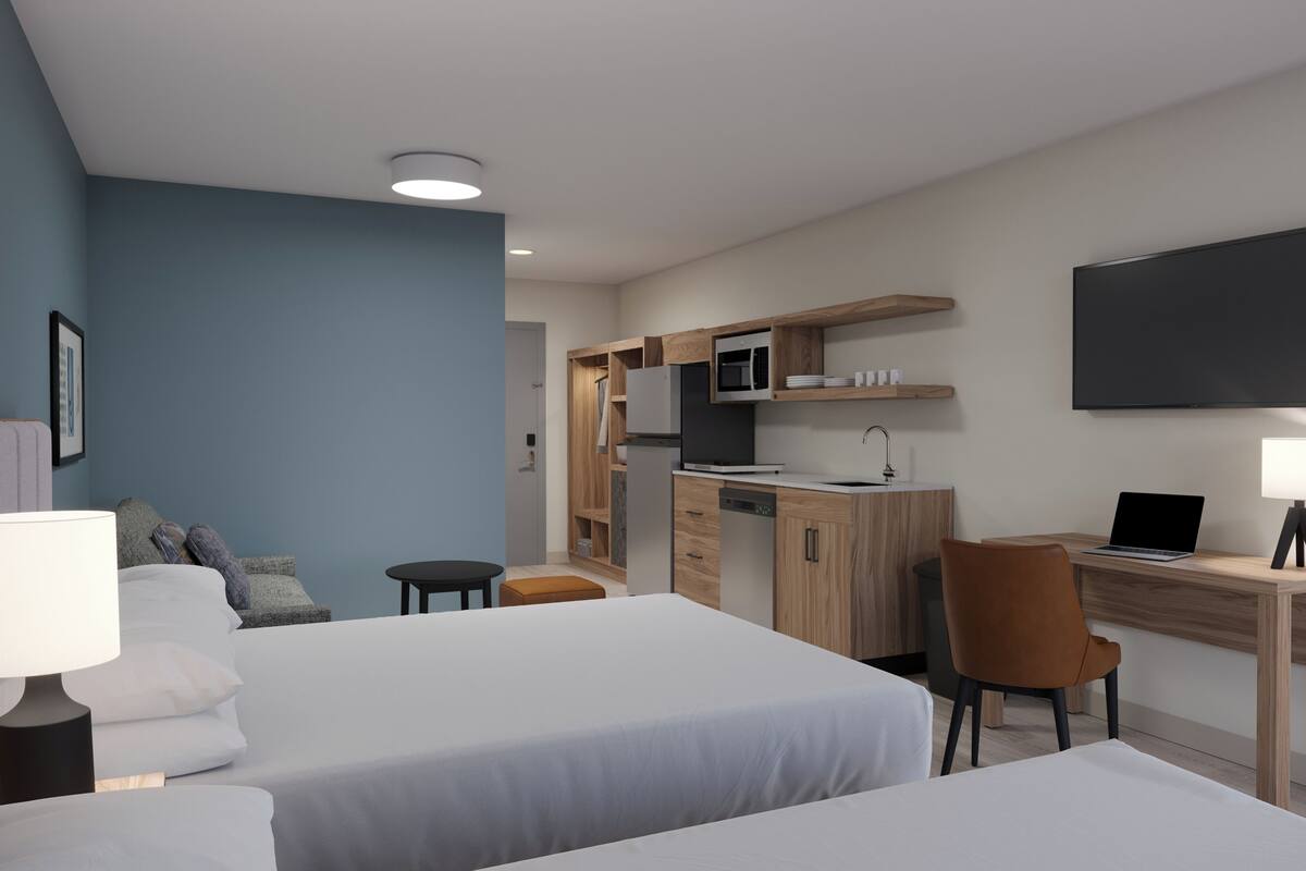 Habitación de hotel con dos camas, un escritorio, una silla, un televisor y una lámpara.