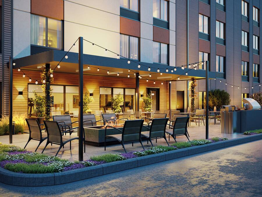 A modern hotel exterior with outdoor seating, a covered patio, and a car parked nearby.