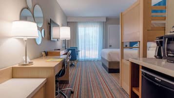 A hotel room with a desk, chair, bed, and a kitchenette.
