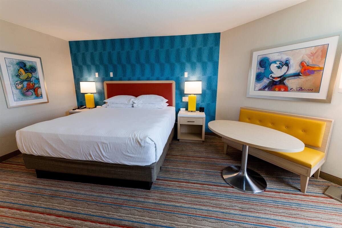 A hotel room with a bed, bedside tables, a small round table, and a sofa.