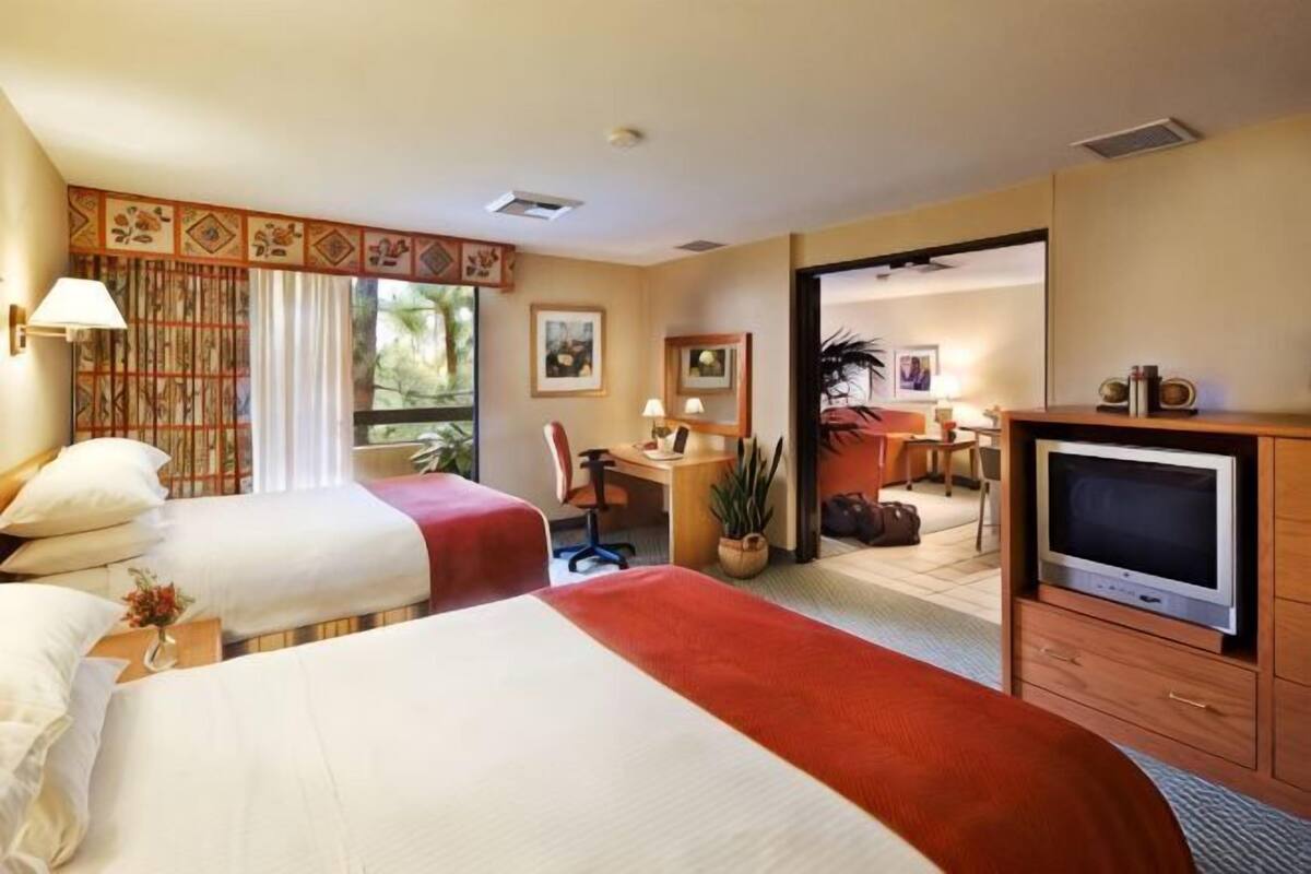 A hotel room with two beds, a desk, a television, and a view of the outdoors.