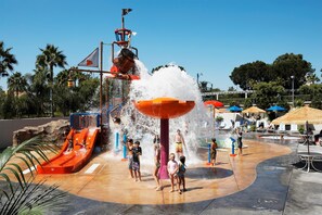 Un parc aquatique comprenant un toboggan aquatique, une grande fontaine et un espace piscine équipé de parasols.