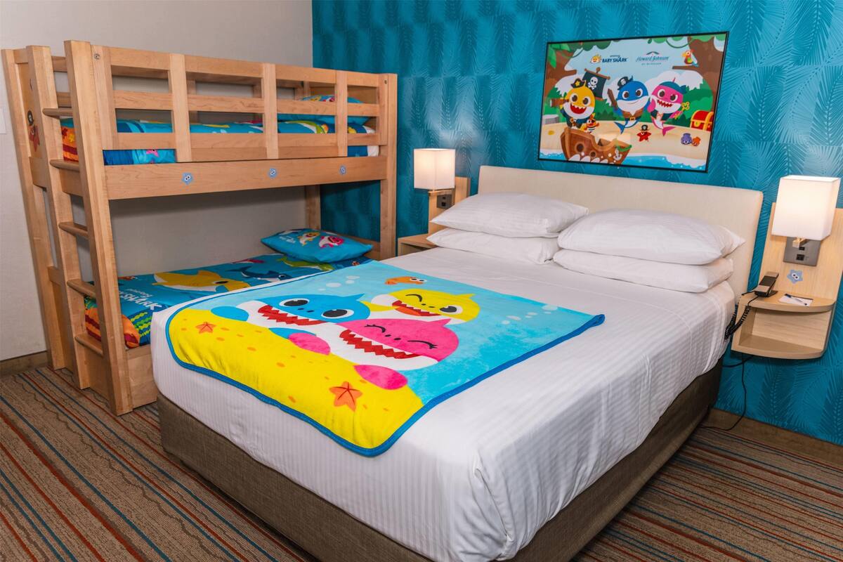 A children's room with bunk beds, a colorful bedspread, and a wall-mounted TV displaying cartoon characters.