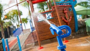 A water play area with a blue water spout and a wooden play structure. - Howard Johnson by Wyndham Anaheim Hotel and Water Playground (Anaheim)