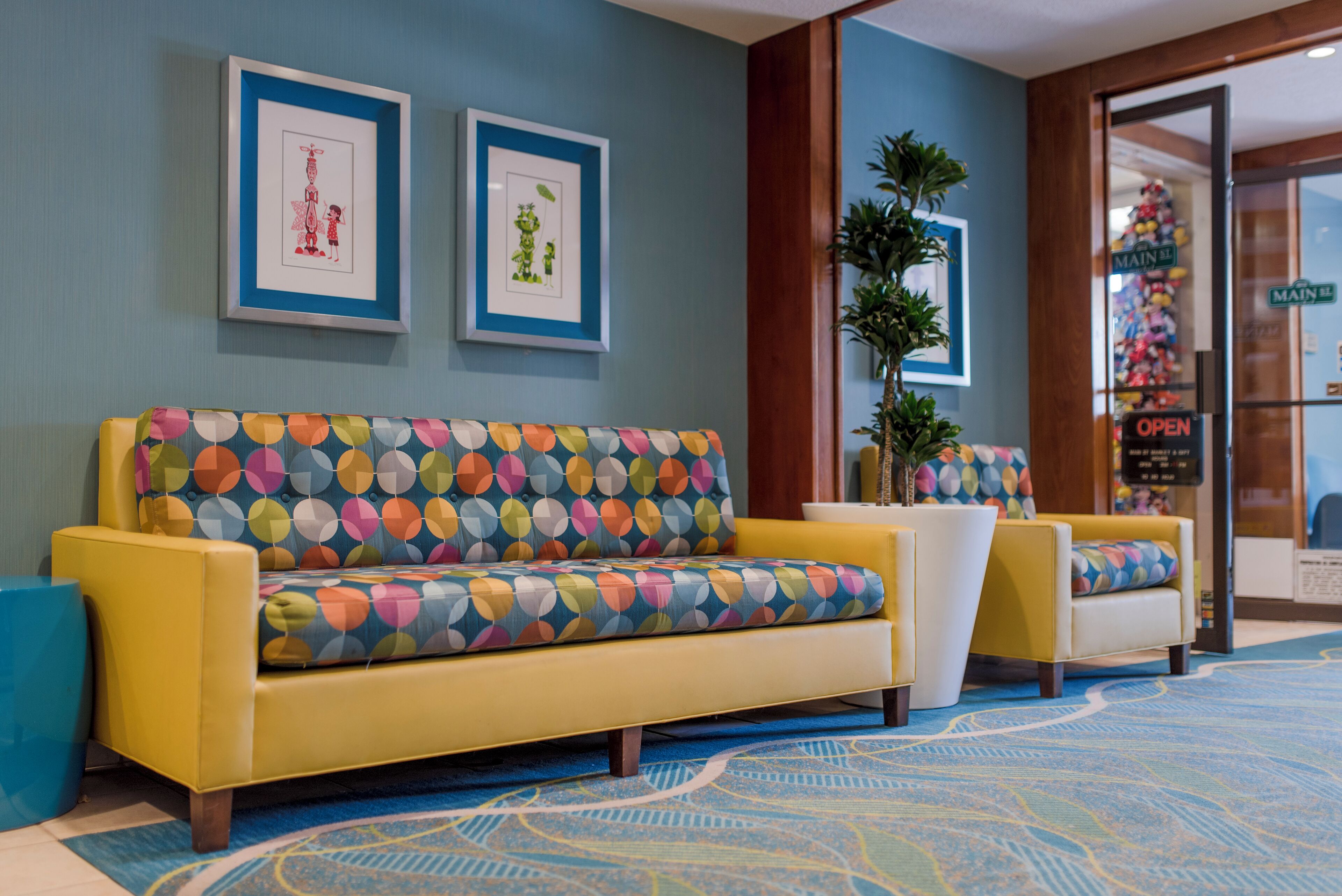 A reception area with a yellow sofa, a colorful patterned couch, and framed artwork on the wall.