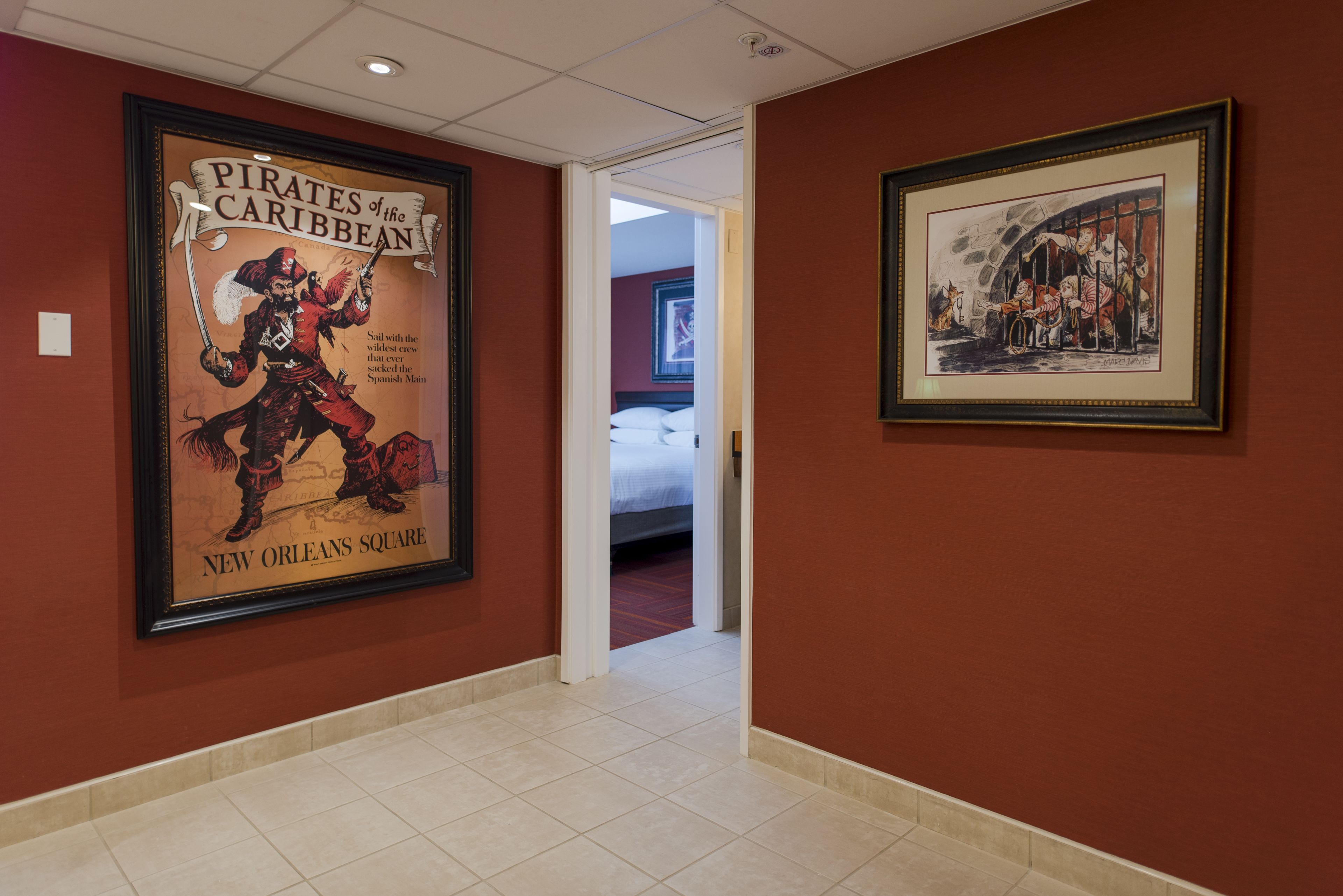 A hallway with a framed poster of a pirate and a framed historical painting.