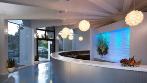 A modern reception area with a curved counter, hanging spherical light fixtures, and a blue-lit wall. - Howard Johnson by Wyndham Anaheim Hotel and Water Playground (Anaheim)