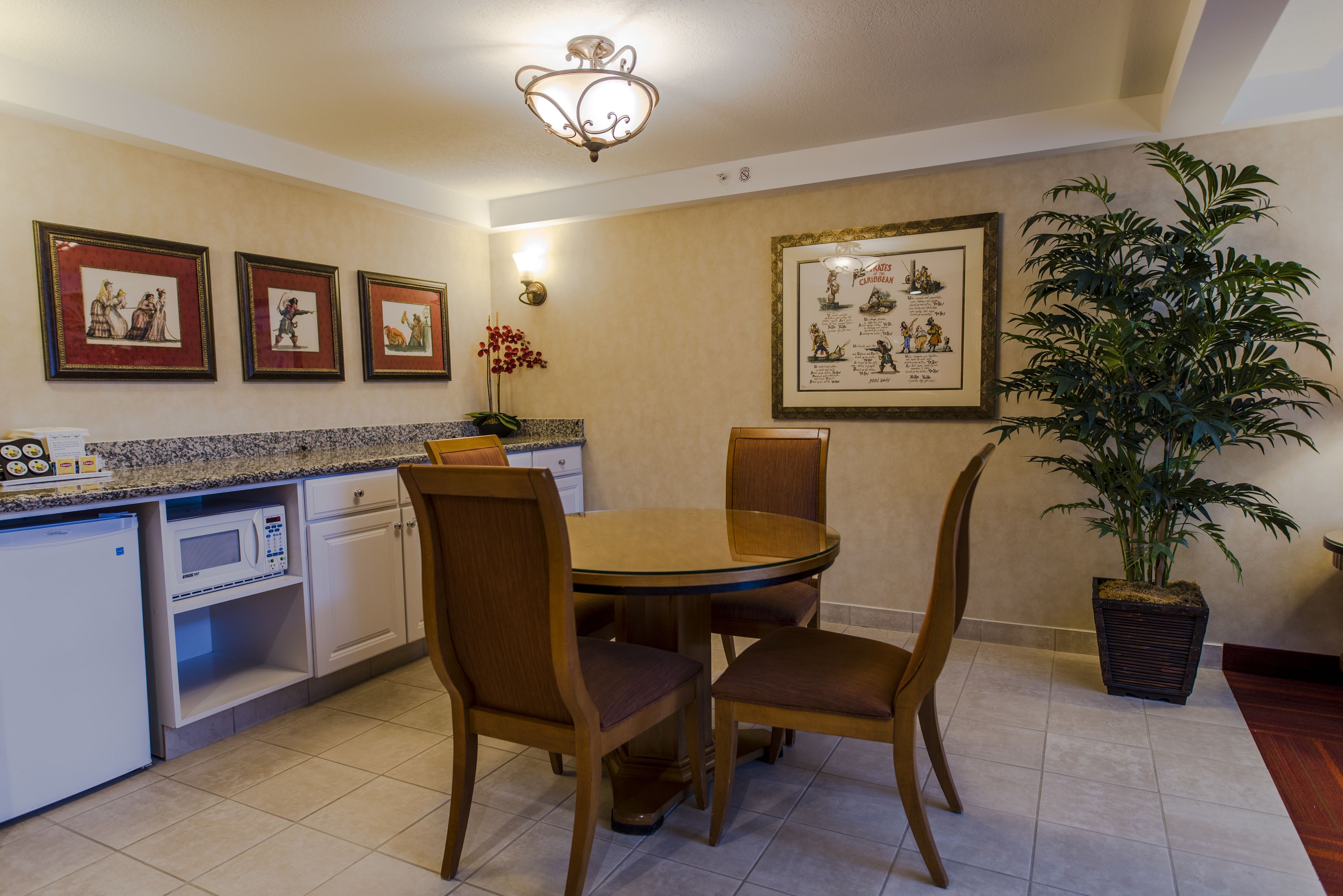 A dining area with a round table, four chairs, a microwave, a refrigerator, and a potted plant.